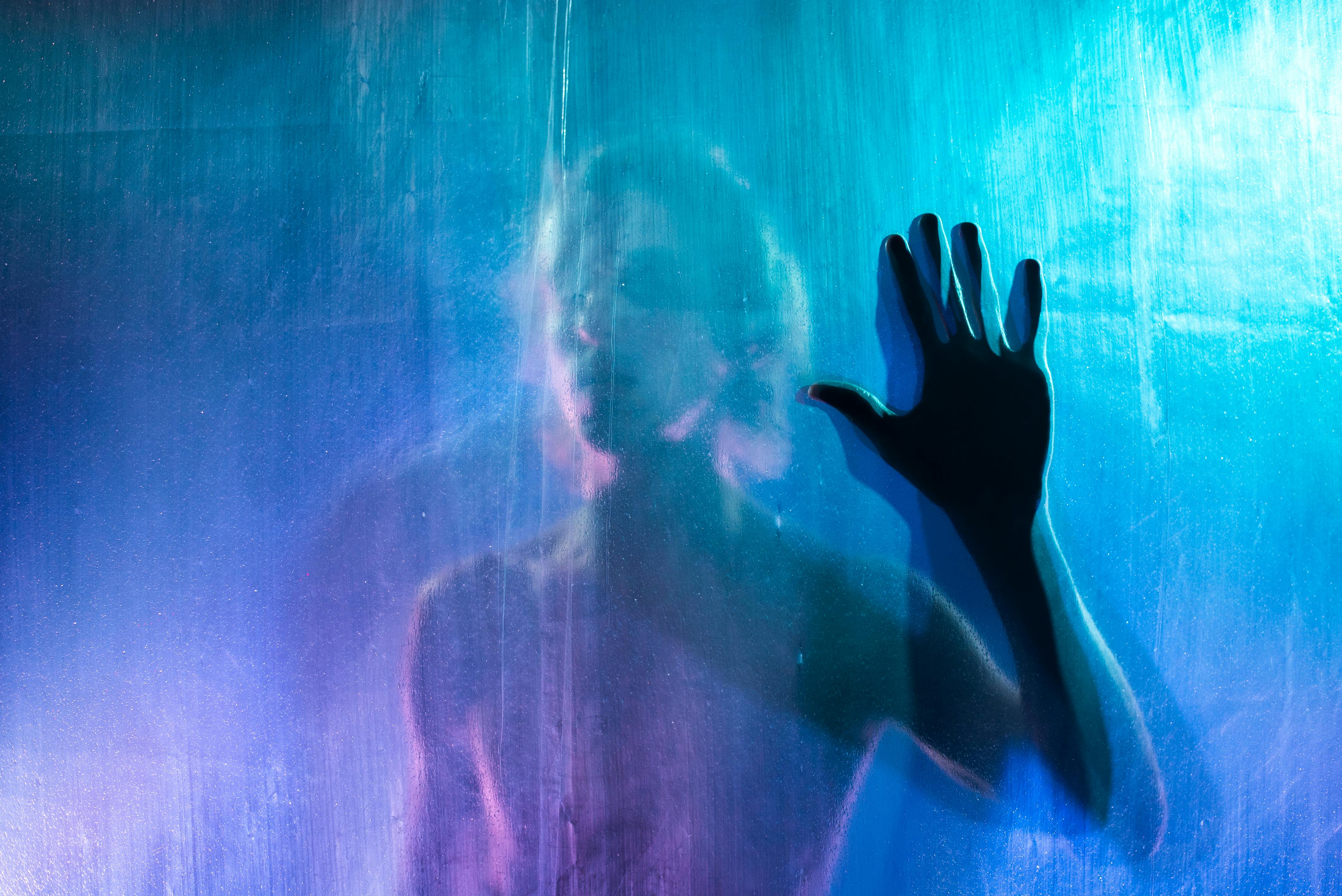 young man pressing his hand against a see through blue film from the other side